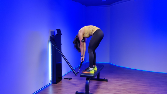 Woman performing a cable Jefferson curl exercise in a gym, standing on a bench and holding a cable bar