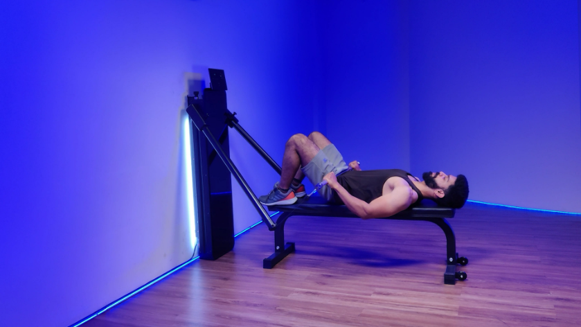 Woman performing a hip thrust exercise with dumbbells on a pink yoga mat in a gym setting