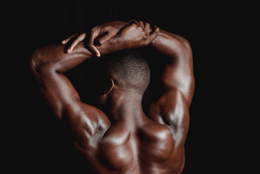 A man flexing his shoulders with his arms raised, showcasing his back muscles.