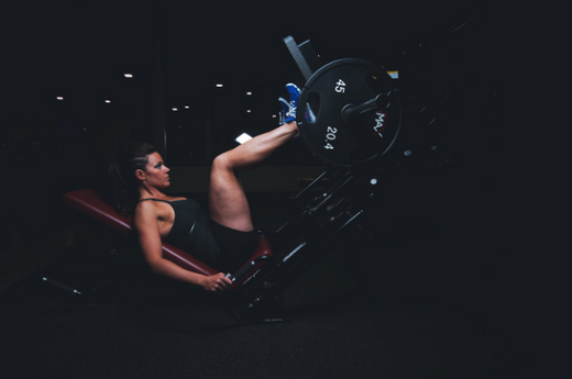 A woman performing circuit weight training on a leg press in a gym.