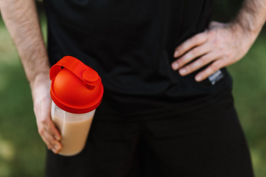 Person holding a shaker bottle with creatine for post workout muscle gain